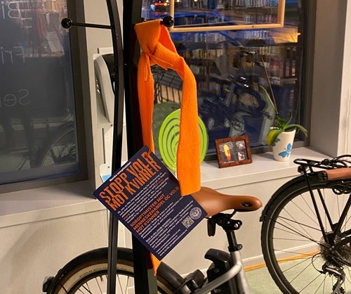 Et oransje bånd med en informasjonsflyer med teksten "Stopp vold mot kvinner" festet til en sykkel. Foto